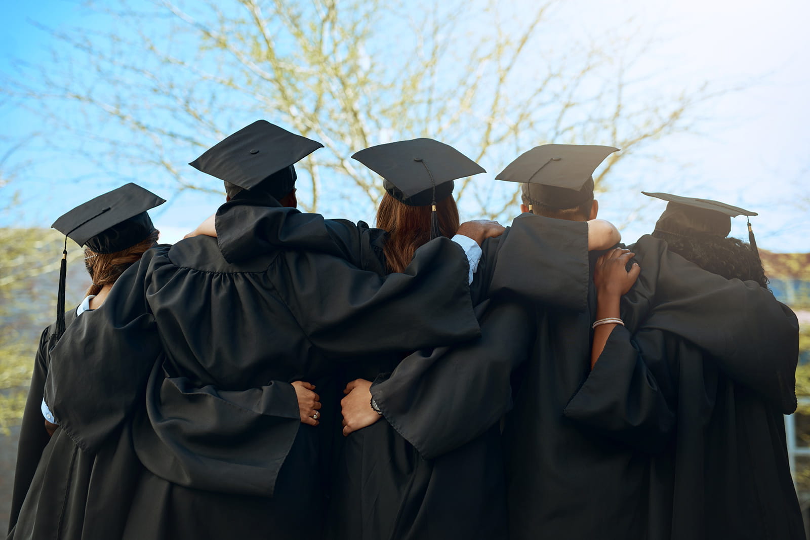 Rearview shot of a group of young students embracing on graduation day